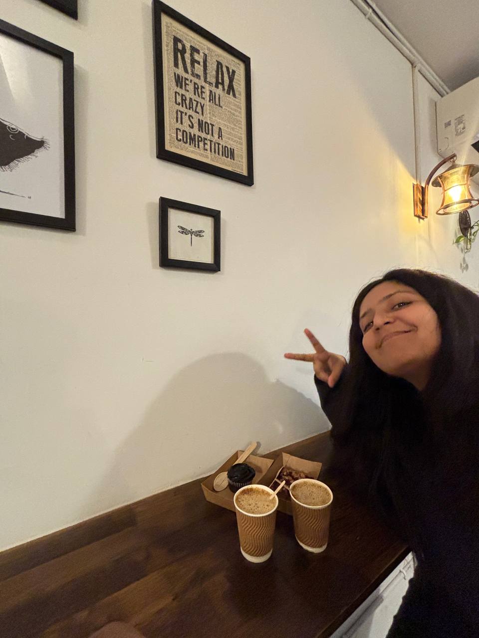 Woman making a peace sign at a cafe table with two hot drinks and desserts